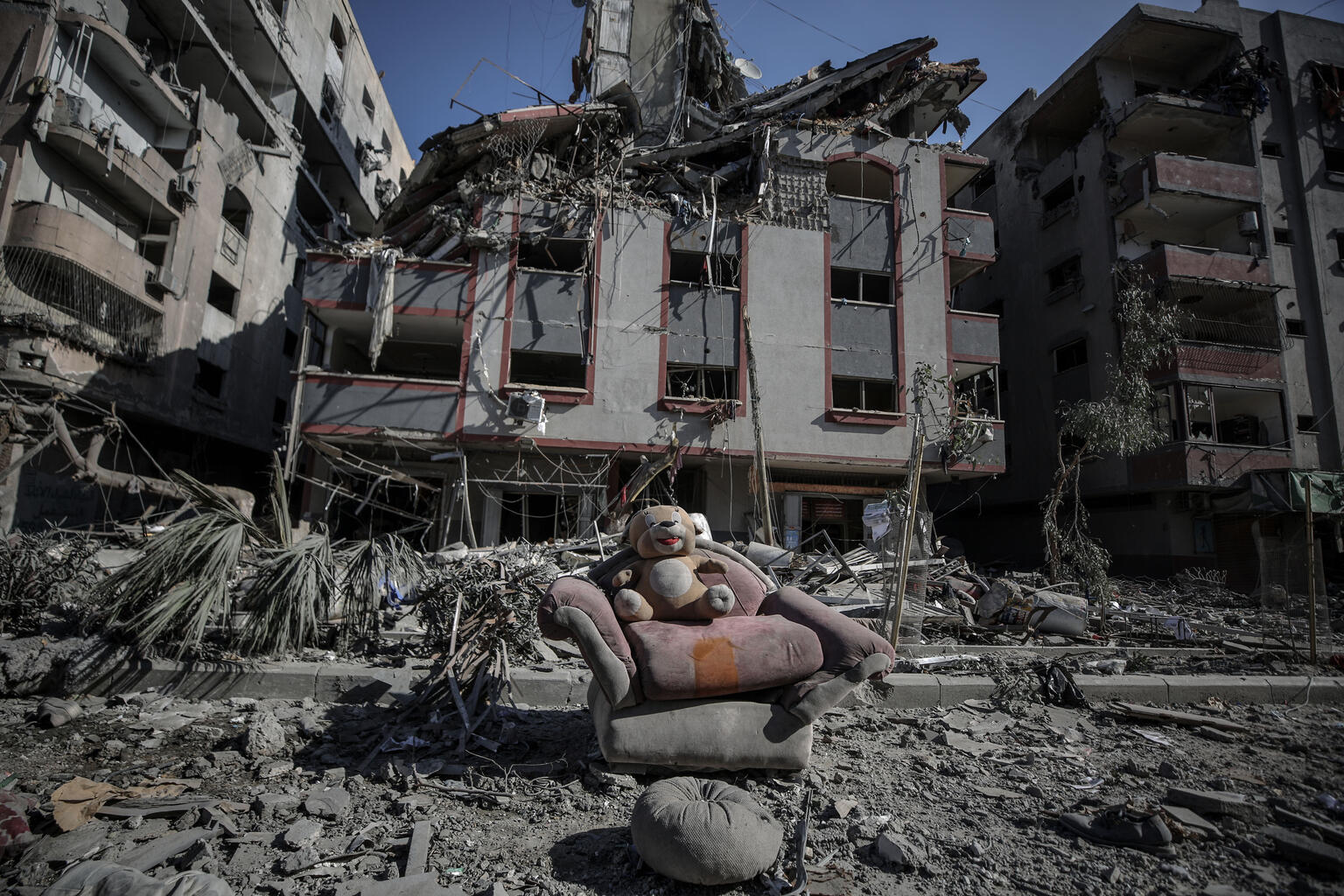 Se ve un juguete de peluche de un niño en un sofá entre escombros en una calle, con edificios dañados al fondo, tras la escalada de hostilidades en la Franja de Gaza, Estado de Palestina.